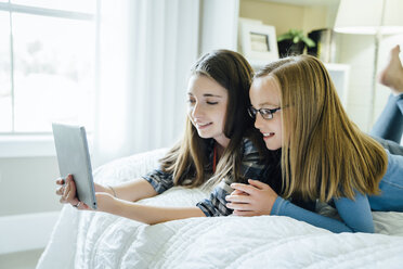 Schwestern, die im Bett liegend einen Tablet-Computer benutzen - CAVF13218