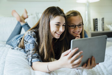 Happy sisters using tablet computer in bedroom - CAVF13221