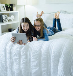 Schwestern, die einen Tablet-Computer benutzen, während sie auf dem Bett im Schlafzimmer liegen - CAVF13222