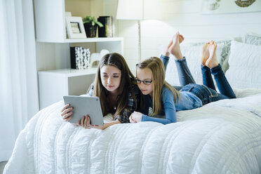 Sisters using tablet computer while lying on bed at home - CAVF13223