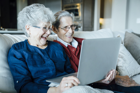 Glückliches älteres Paar, das auf dem Sofa sitzend Videokonferenzen über einen Laptop abhält, lizenzfreies Stockfoto