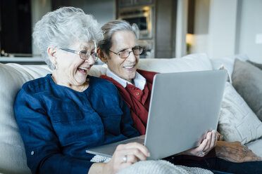 Happy senior couple video conferencing through laptop computer while sitting on sofa - CAVF13229