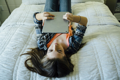 Teenager-Mädchen, das einen Tablet-Computer benutzt, während es auf dem Bett liegt - CAVF13235