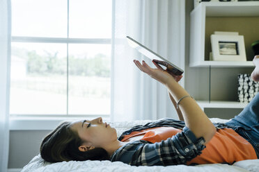 Seitenansicht eines Teenagers, der einen Tablet-Computer benutzt, während er zu Hause auf dem Bett liegt - CAVF13237