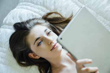 High angle view of teenage girl using tablet computer while lying on bed at home - CAVF13238