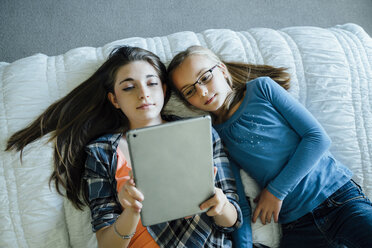 Hochformatige Ansicht von Schwestern, die einen Tablet-Computer benutzen, während sie zu Hause auf dem Bett liegen - CAVF13239