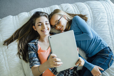 High angle view of happy sisters using tablet computer while lying on bed at home - CAVF13240