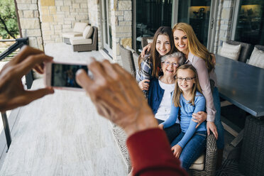 Abgeschnittene Hände eines älteren Mannes, der eine glückliche Familie auf einer Veranda mit seinem Smartphone fotografiert - CAVF13248