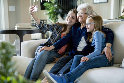 Glückliche Großmutter und Enkeltöchter nehmen Selfie durch Smartphone, während auf dem Sofa sitzen - CAVF13263