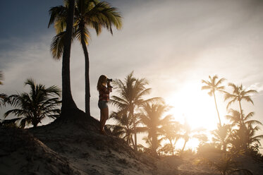 Frau beim Fotografieren unter Palmen an einem sonnigen Tag - CAVF13268