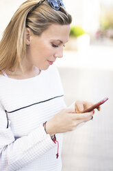 Woman using mobile phone while standing on footpath - CAVF13287