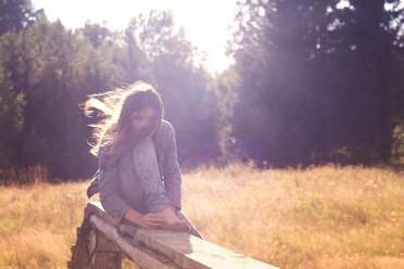 Mädchen sitzt auf einer Struktur auf einem Feld an einem sonnigen Tag - CAVF13290