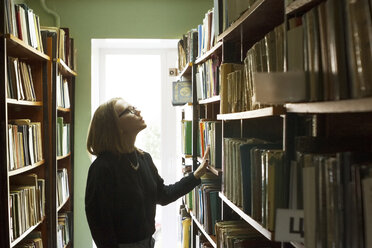 Seitenansicht einer Frau, die in einer Bibliothek steht und Bücher auswählt - CAVF13294