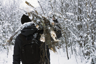 Mann trägt einen Holzstapel auf der Schulter, während er im Winter an kahlen Bäumen vorbeigeht - CAVF13298