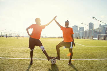 Porträt einer glücklichen Sportlerin, die mit einem Fußball auf einem Feld bei strahlendem Sonnenschein 