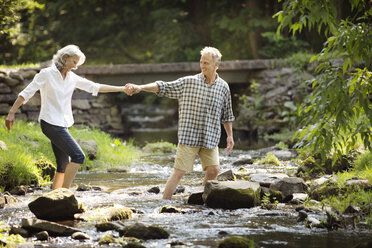 Senior man assisting woman while crossing stream - CAVF13695