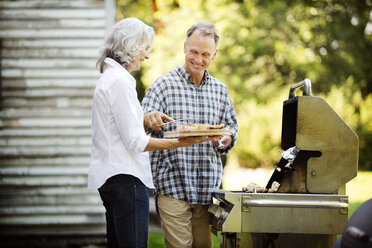 Glückliches älteres Ehepaar bereitet Essen zu, während es am Grill im Hinterhof steht - CAVF13700