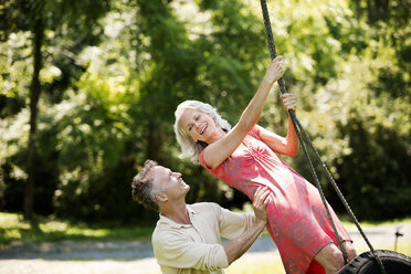 Fröhliches älteres Paar spielt auf einer Schaukel im Park - CAVF13724