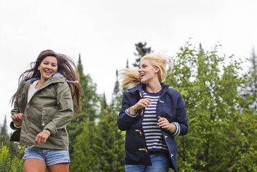 Happy female friends running against trees - CAVF13741