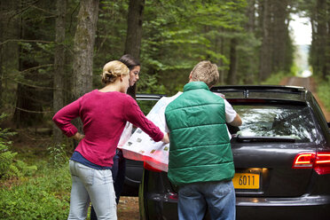 Freunde lesen eine Karte, während sie neben einem Auto im Wald stehen - CAVF13745