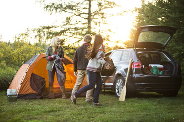 Glückliche Freunde bereiten ihr Zelt im Auto auf einem Feld im Wald vor - CAVF13748