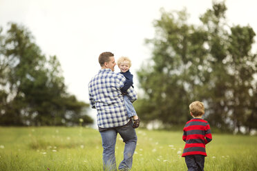 Happy father with sons on grassy field - CAVF13760