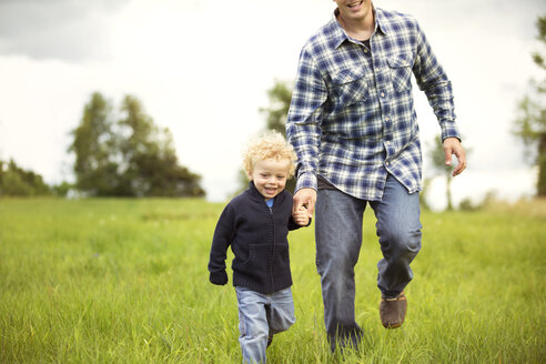 Glücklicher Vater und Sohn beim Spaziergang auf einer Wiese - CAVF13762