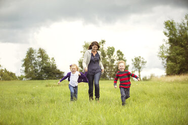 Happy mother walking with children on grassy field against sky - CAVF13763