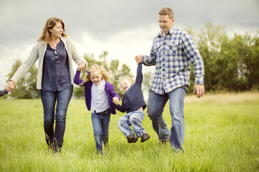 Happy children with parents enjoying on grassy field - CAVF13766