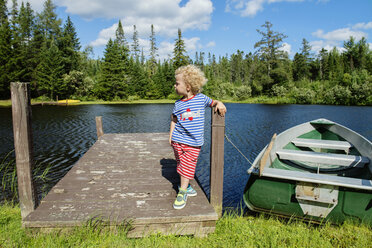 Boy standing on jetty by moored boat at lakeshore - CAVF13775