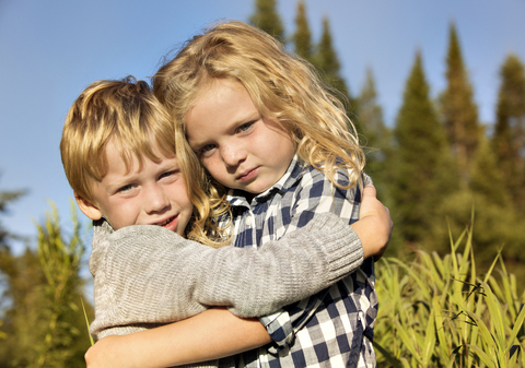 Porträt von Geschwistern, die sich auf einem Feld an einem sonnigen Tag umarmen, lizenzfreies Stockfoto