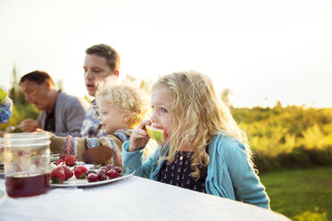 Girl eating watermelon with family on picnic table - CAVF13814