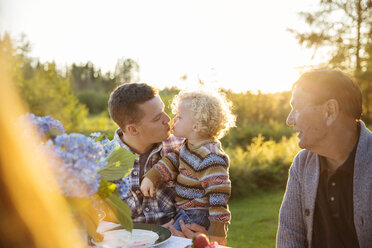 Vater küsst Sohn am Picknicktisch an einem sonnigen Tag - CAVF13818