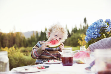 Boy eating watermelon on picnic table against clear sky - CAVF13828