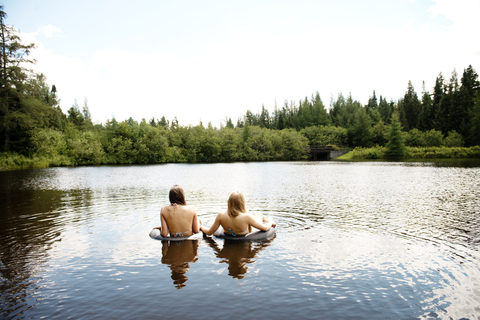 Rückansicht von Freundinnen beim Schwimmen im See gegen den Himmel, lizenzfreies Stockfoto