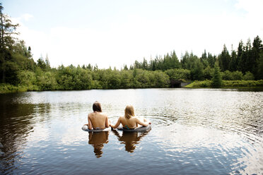 Rear view of female friends swimming on lake against sky - CAVF13839