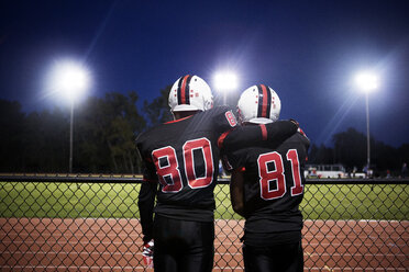 Rear view of American football players standing against illuminated field - CAVF13863