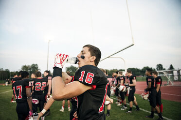 Boy drinking water on American football field against sky - CAVF13867