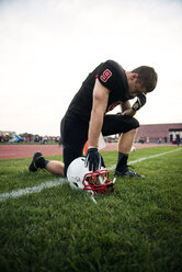 Männlicher American-Football-Spieler kniend auf einem Grasfeld vor dem Himmel - CAVF13868