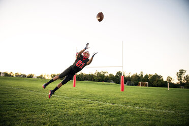 Young man diving to catch American football at playing field against sky - CAVF13880