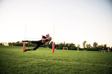 Junger Mann fängt American Football auf Feld gegen Himmel - CAVF13881