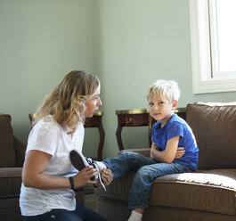 Mother assisting son in wearing shoes at home - CAVF13885