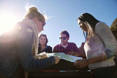 Low angle view of friends looking at map against sky on sunny day - CAVF13908
