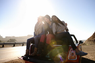 Freundinnen sitzen auf Auto gegen Himmel - CAVF13909