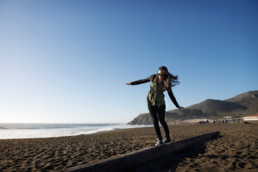 Frau geht auf einem Baumstamm am Strand gegen den klaren Himmel - CAVF13913