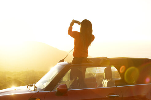 Rückansicht einer Frau, die auf dem Sonnendach eines Autos steht und fotografiert - CAVF13930
