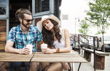 Glückliches Paar hält Einwegbecher und sitzt am Tisch eines Straßencafés - CAVF13949