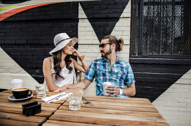 Young couple talking while sitting by table at sidewalk cafe - CAVF13950