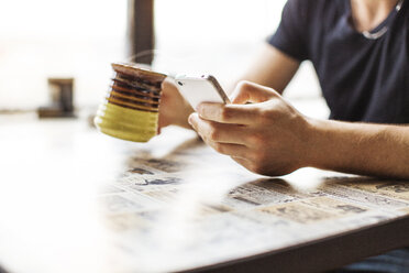 Abgeschnittenes Bild eines Mannes, der sein Smartphone benutzt, während er auf dem Tisch Kaffee trinkt - CAVF13962