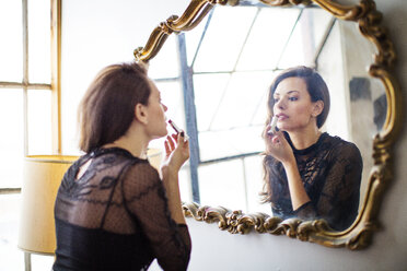 Woman looking at mirror and applying lipstick at home - CAVF13972